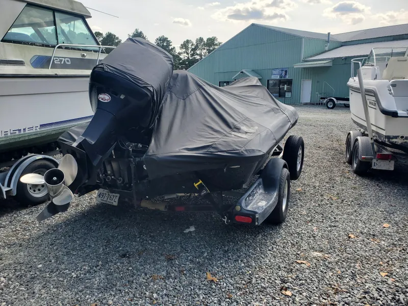 Slide: The Image of 2003 Ranger 185 VX/VS boat covered, parked on gravel, with nearby boats and a building. - 7