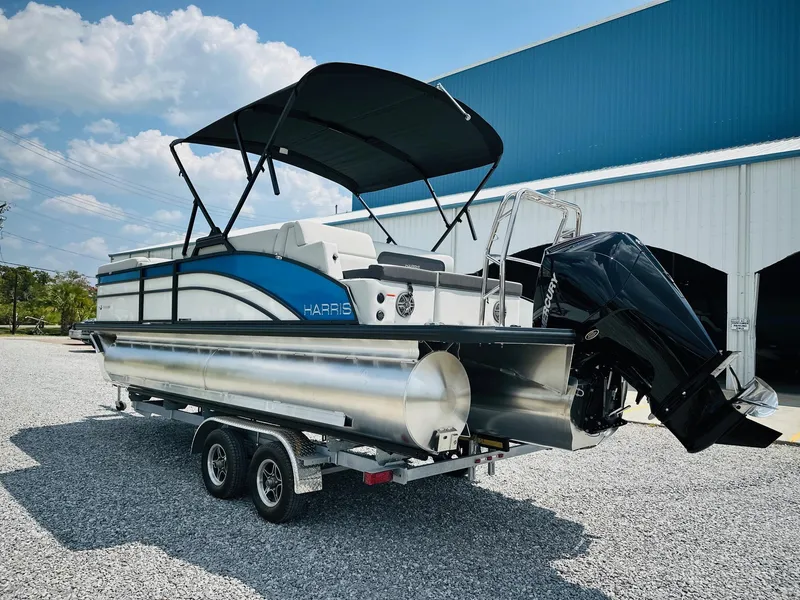 Slide: The Image of 2025 Harris Cruiser 230 pontoon boat on trailer, parked outdoors near a blue building. - 4