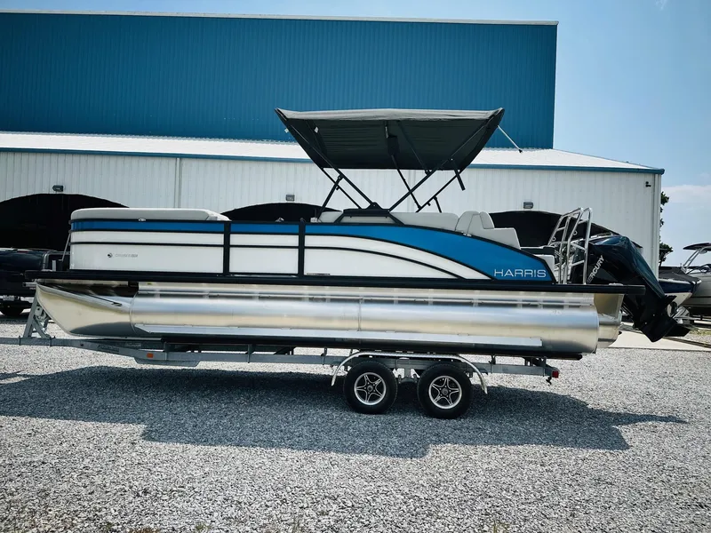 Slide: The Image of 2025 Harris Cruiser 230 pontoon boat on trailer, parked outdoors near a blue building. - 5