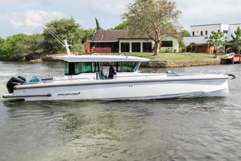Slide: The Image of 2024 Axopar 37XC CROSS CABIN boat cruising on a calm river near houses. - 1