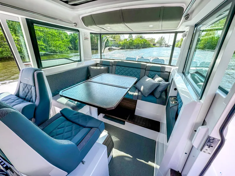 Slide: The Image of 2024 Axopar 37XC CROSS CABIN interior with blue seating and table, overlooking a scenic waterway. - 10