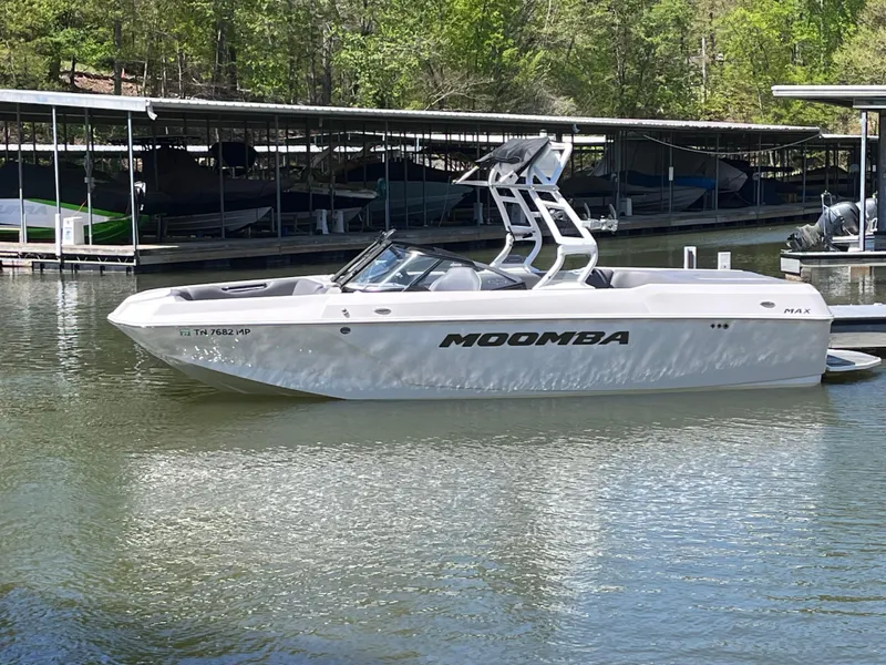 Slide: The Image of 2024 Moomba Max boat docked on a calm lake with trees in the background. - 1