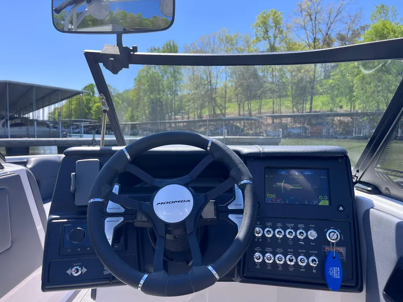 Slide: The Image of 2024 Moomba Max boat dashboard with steering wheel and control panel, docked by a scenic lake. - 15