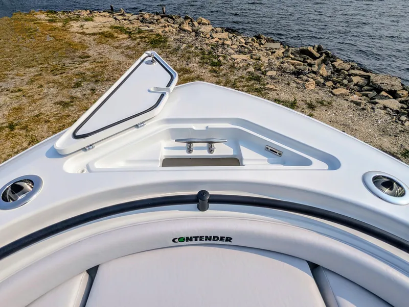 Slide: The Image of 2025 Contender 24 Sport boat bow with open hatch, near rocky shoreline. - 10