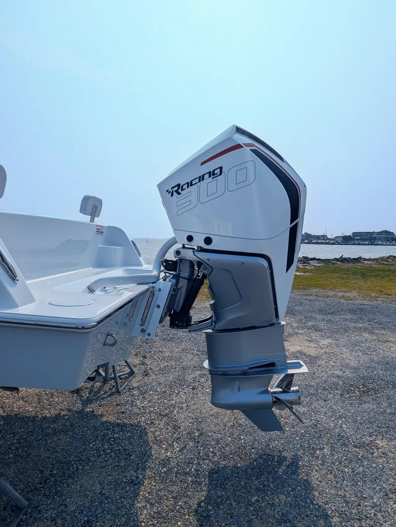 Slide: The Image of 2025 Contender 24 Sport boat with powerful outboard motor, parked on gravel near water. - 20