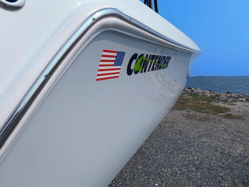 Slide: The Image of 2025 Contender 24 Sport boat with American flag decal by the shore. - 24