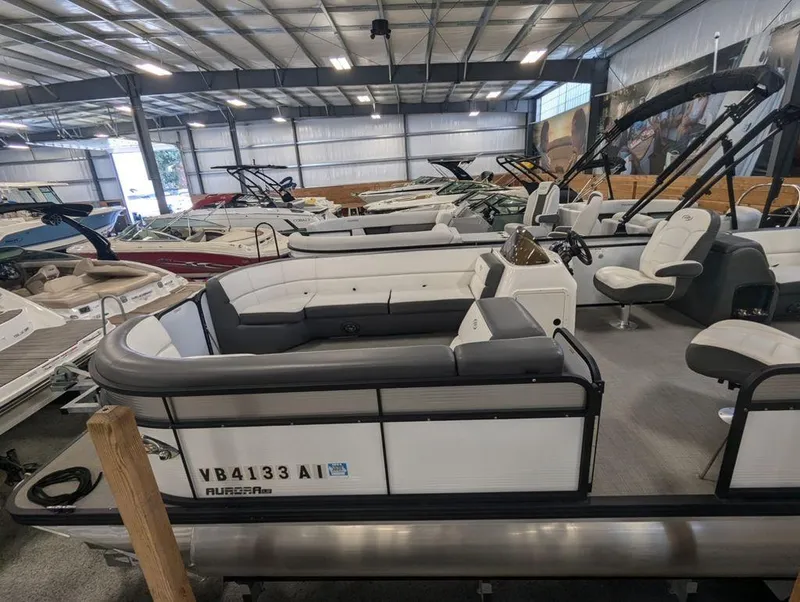 Slide: The Image of 2022 Manitou 23 Aurora LE RF VP pontoon boat in showroom, surrounded by other boats. - 1