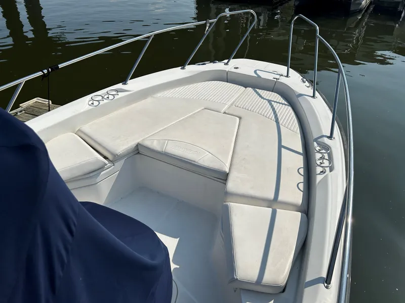 Slide: The Image of 2013 Boston Whaler 230 Dauntless boat with cushioned seating, docked on calm water. - 16