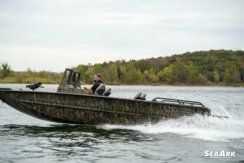 Slide: The Image of 2025 SeaArk Predator boat cruising on a lake with scenic forested background. - 32
