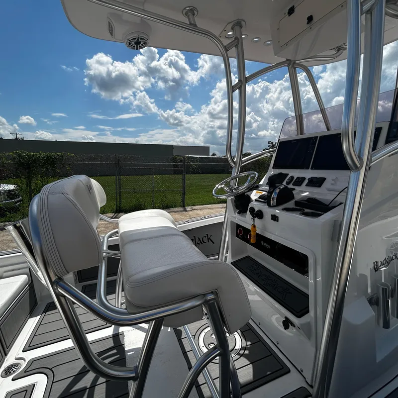 Slide: The Image of 2021 BlackJack 256 Bay boat interior with helm and seating under a sunny sky. - 17