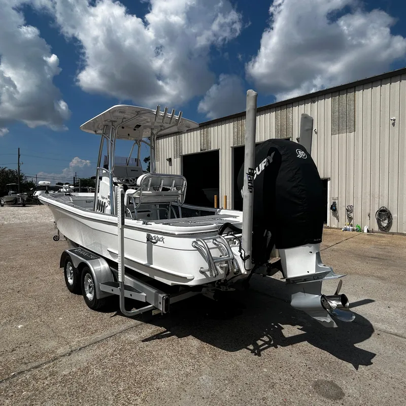 Slide: The Image of 2021 BlackJack 256 Bay boat on trailer, parked outside a warehouse under a cloudy sky. - 6