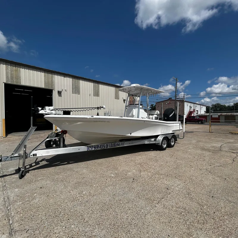 Slide: The Image of 2021 BlackJack 256 Bay boat on trailer outside industrial building under blue sky. - 8