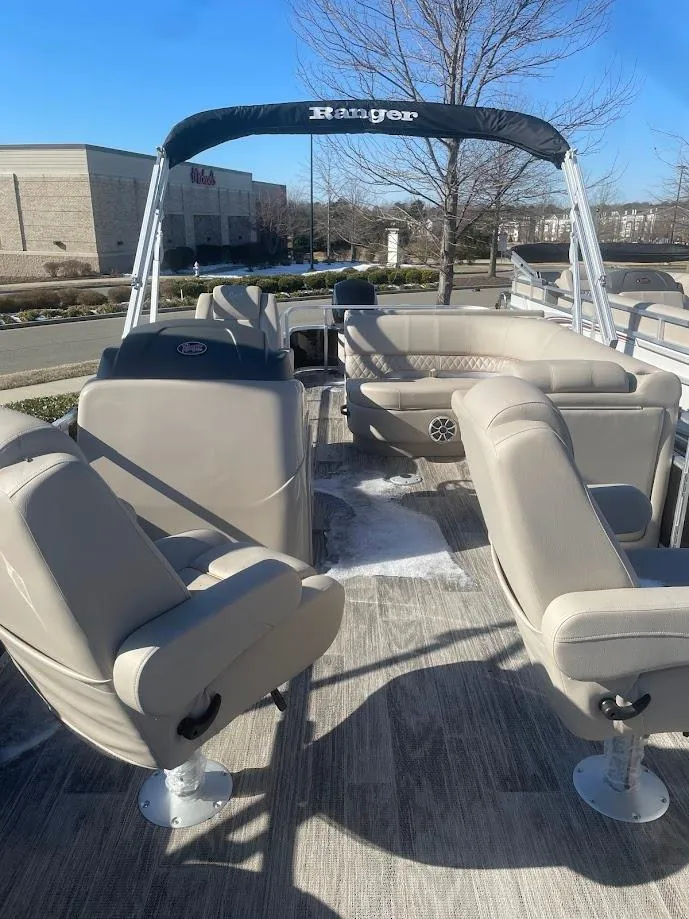 Slide: The Image of 2024 Ranger Reata 220F pontoon boat with beige seating and canopy, parked outdoors. - 1