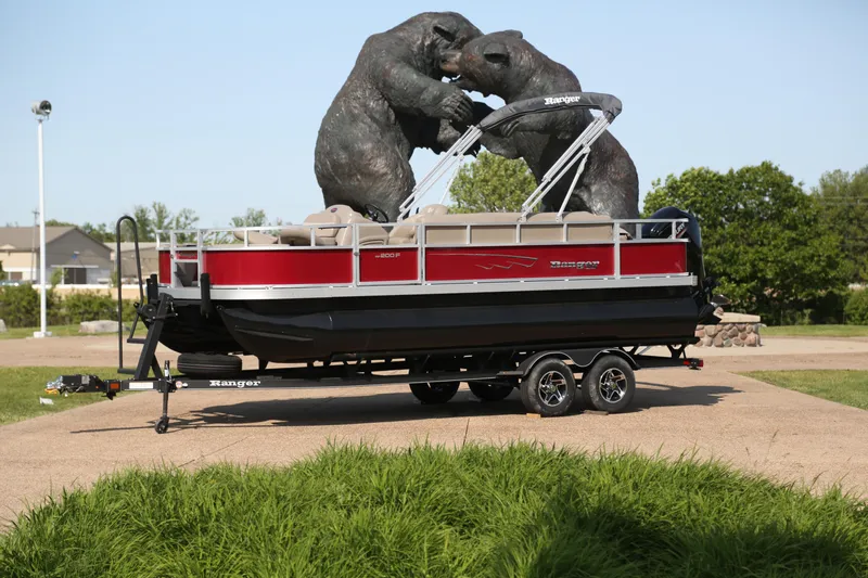 The Image of 2024 Ranger Reata 200F pontoon boat on trailer, red and black design, outdoor setting. - 0
