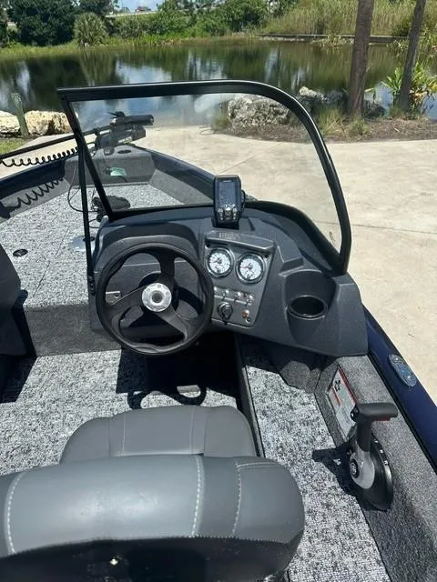 Slide: The Image of 2025 Bass Tracker PGV16WT boat interior with steering wheel and dashboard by a lake. - 5