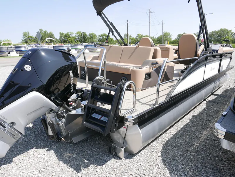 Slide: The Image of 2025 Barletta Cabrio 24UC pontoon boat with Mercury outboard engine, parked on gravel. - 2