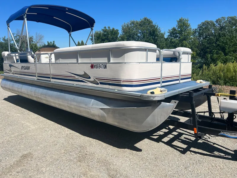 Slide: The Image of 2003 Sylvan Mirage pontoon boat with blue canopy on a trailer, parked outdoors. - 11