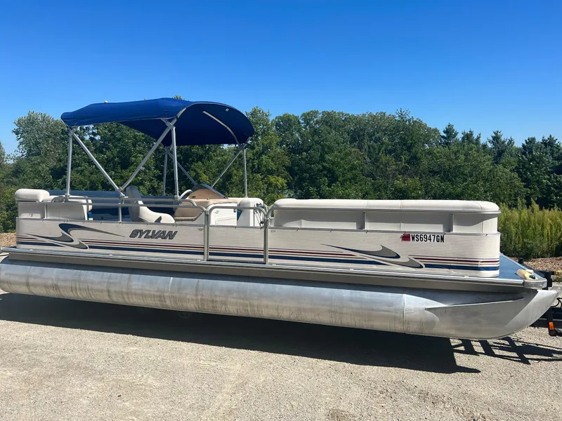 Slide: The Image of 2003 Sylvan Mirage pontoon boat with blue canopy, parked on a sunny day. - 12