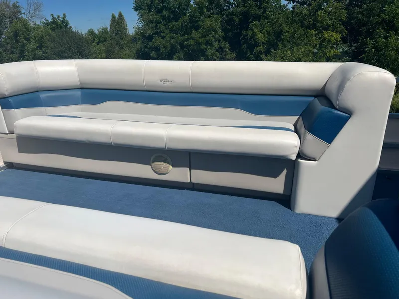 Slide: The Image of 2003 Sylvan Mirage boat interior with white and blue seating, surrounded by lush greenery. - 7