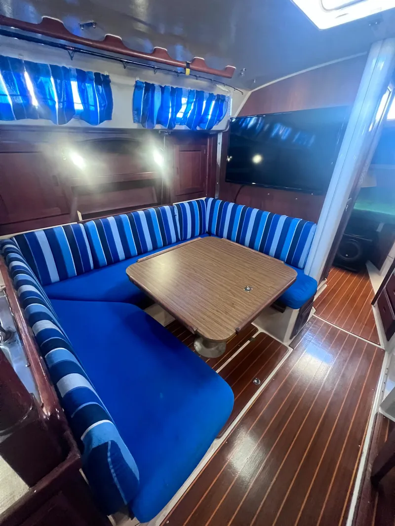 Slide: The Image of 1983 Catalina 36 yacht interior with blue-striped seating and wooden table. - 29