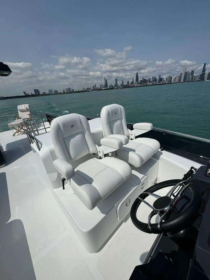 Slide: The Image of 2022 Sirena 58 Flybridge yacht with white captain chairs, city skyline in background. - 33