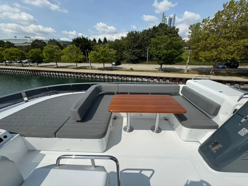 Slide: The Image of Sirena 58 Flybridge 2022 yacht deck with seating and table, docked by a tree-lined shore. - 47