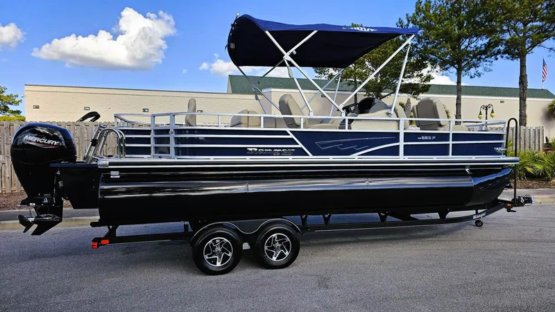 Slide: The Image of 2024 Ranger Reata 223F pontoon boat with canopy on trailer, parked outdoors. - 0