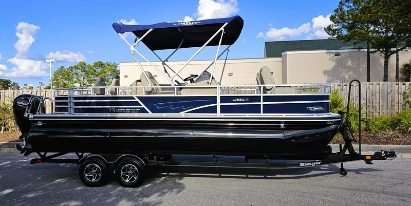 Slide: The Image of 2024 Ranger Reata 223F pontoon boat with canopy on trailer, parked outdoors. - 1