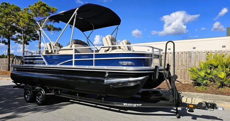 Slide: The Image of 2024 Ranger Reata 223F pontoon boat on trailer, parked outdoors under blue sky. - 3