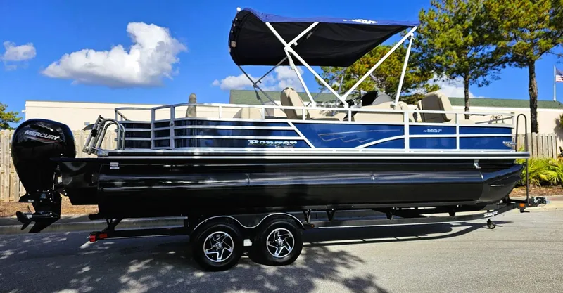Slide: The Image of 2024 Ranger Reata 223F pontoon boat with canopy on trailer, parked outdoors. - 8