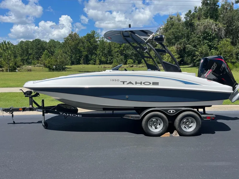 The Image of 2024 Tahoe 1950 boat on trailer, parked on road, surrounded by trees and blue sky. - 0