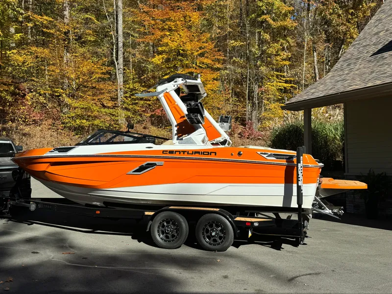 Slide: The Image of 2023 Centurion Ri230 boat in vibrant orange, parked on a trailer in a wooded area. - 11