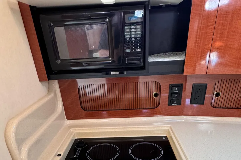 Slide: The Image of 2004 Sea Ray 320 Sundancer kitchen with microwave, stove, and wooden cabinetry. - 17