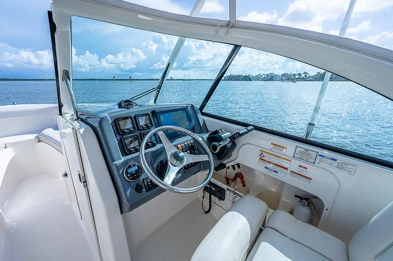 Slide: The Image of 2014 Pursuit DC 265 Dual Console boat interior with steering wheel and dashboard, overlooking water. - 21