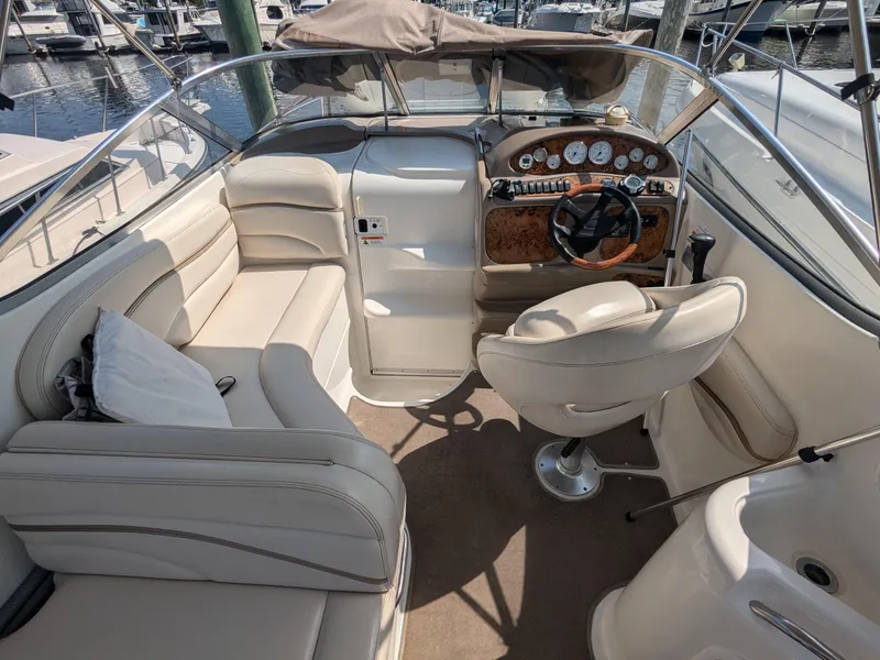 Slide: The Image of 2004 Larson Cabrio 260 boat interior with beige seating and wood-accented dashboard. - 10