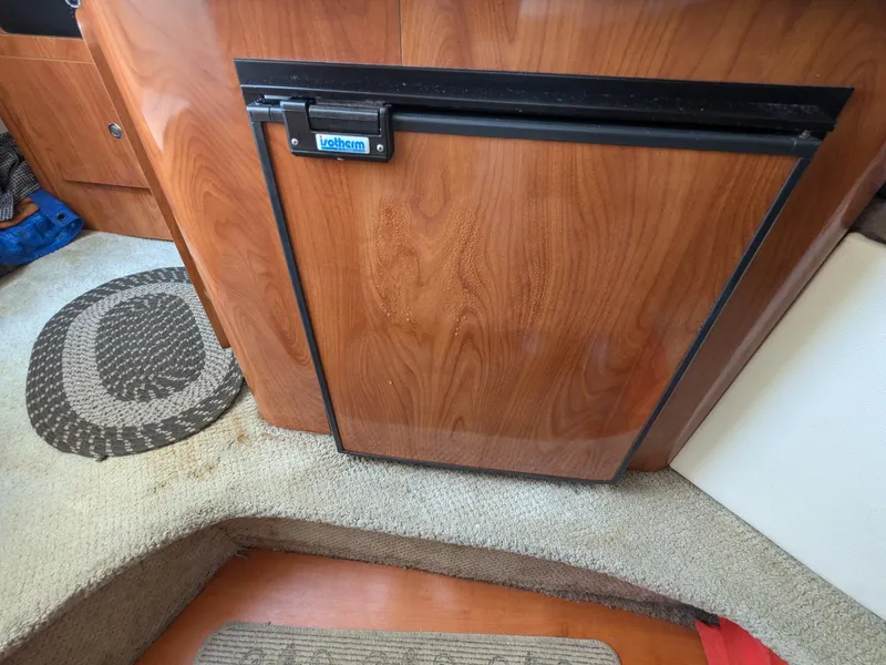 Slide: The Image of 2004 Larson Cabrio 260 interior with wood paneling and compact fridge. - 18