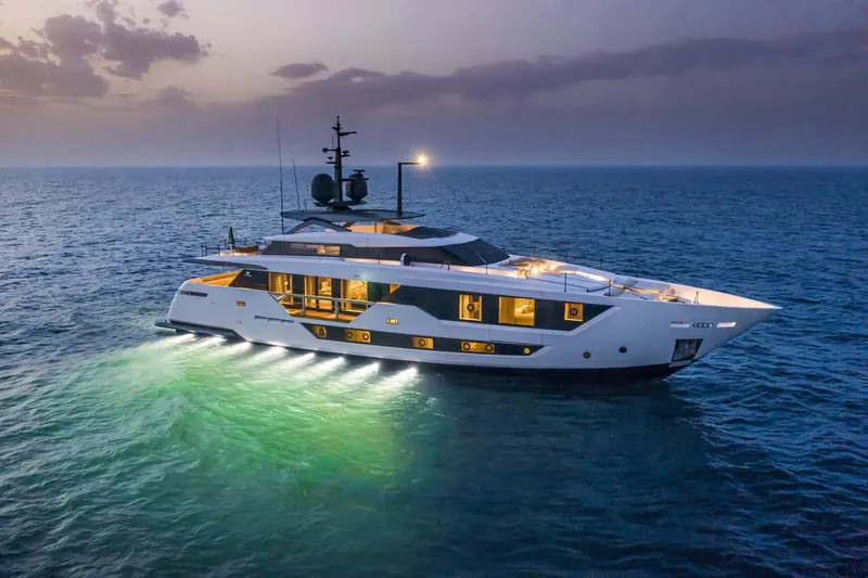 Slide: The Image of Luxurious 2023 Custom Line 106' yacht illuminated on serene ocean at dusk. - 1