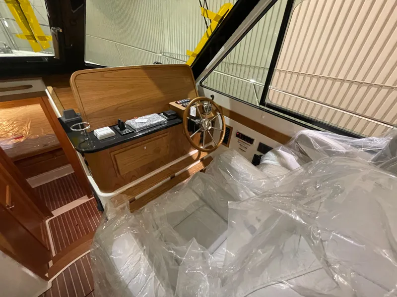 Slide: The Image of 2025 Back Cove 372 boat interior with wooden helm, steering wheel, and plastic-covered seating. - 32