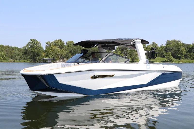 Slide: The Image of 2025 Nautique G25 boat on a calm lake with trees in the background. - 0