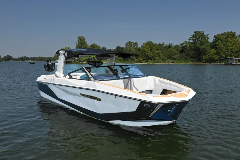 Slide: The Image of 2025 Nautique G25 boat on a serene lake with lush green shoreline. - 1