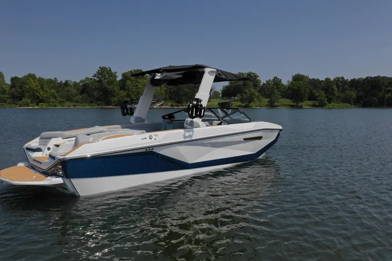 Slide: The Image of 2025 Nautique G25 boat on a serene lake with lush green shoreline. - 2