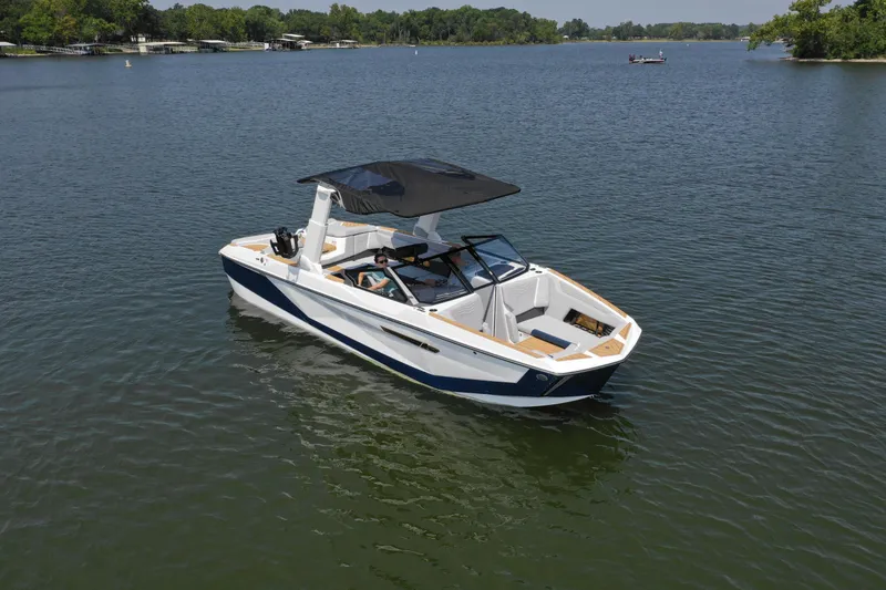 Slide: The Image of 2025 Nautique G25 boat on a calm lake with lush green shoreline. - 5