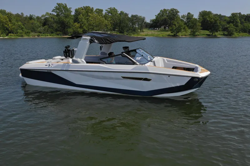 Slide: The Image of 2025 Nautique G25 boat on a serene lake with lush green trees. - 7
