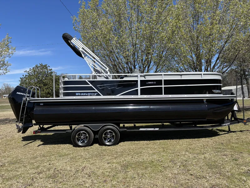 Slide: The Image of 2024 Ranger 223C pontoon boat on trailer, parked on grass with trees in background. - 1
