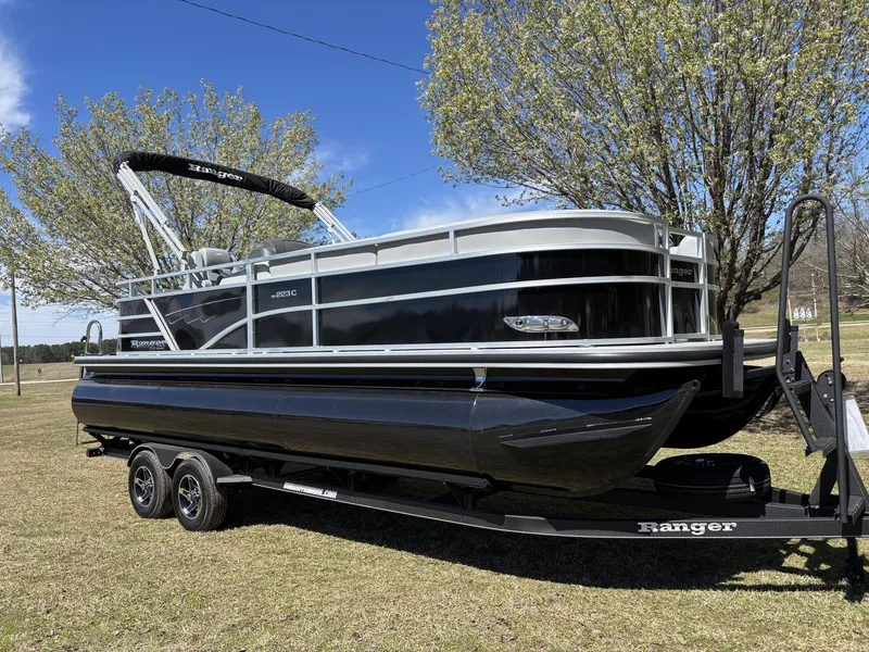 Slide: The Image of 2024 Ranger 223C pontoon boat on trailer, parked on grass with trees in background. - 4