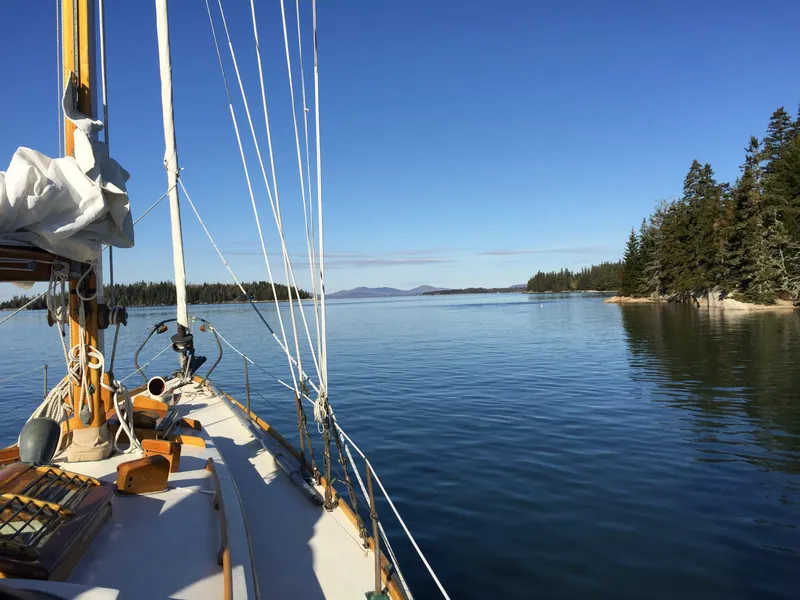 Slide: The Image of 1964 Concordia 41 Yawl sailing on calm waters near a forested shoreline under clear blue skies. - 14