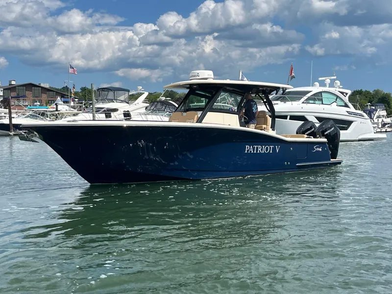 Slide: The Image of 2024 Scout 330 LXF boat on water, blue hull, sunny day, marina background. - 2