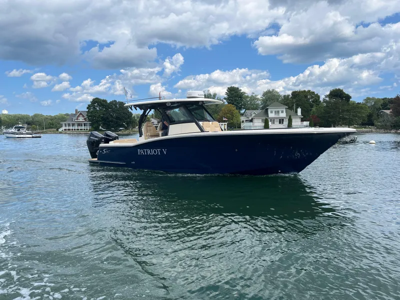 Slide: The Image of 2024 Scout 330 LXF boat on water, clear sky, waterfront homes in background. - 3