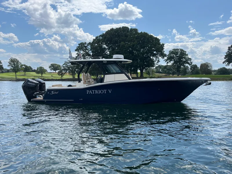 Slide: The Image of 2024 Scout 330 LXF boat on a lake with trees in the background. - 6