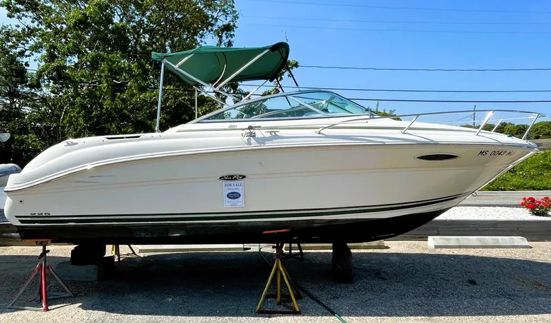 Slide: The Image of 2001 Sea Ray 225 Weekender boat on stands, white hull, green canopy, outdoor setting. - 0